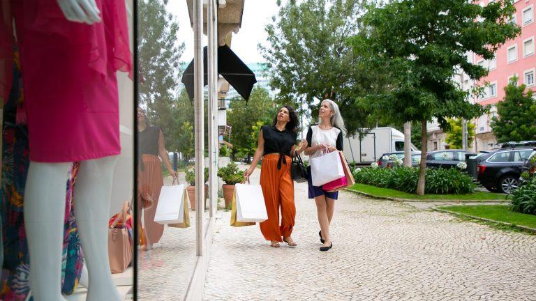 שתי נשים עם שקיות קניות מהלכות לאורך חנויות ברחוב פתוח